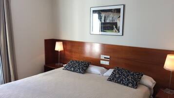 A hotel room with a large bed, two bedside lamps, a nightstand, a wall-mounted picture, and a window with curtains.