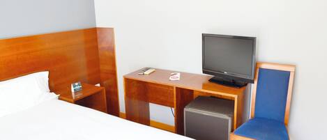A hotel room with a bed, a desk with a television, a small refrigerator, and a chair.