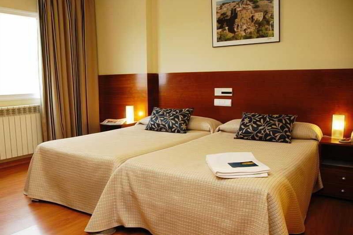 Ein Hotelzimmer mit zwei Betten, einem hölzernen Kopfteil, einem Bild an der Wand und einem Fenster mit Vorhängen.