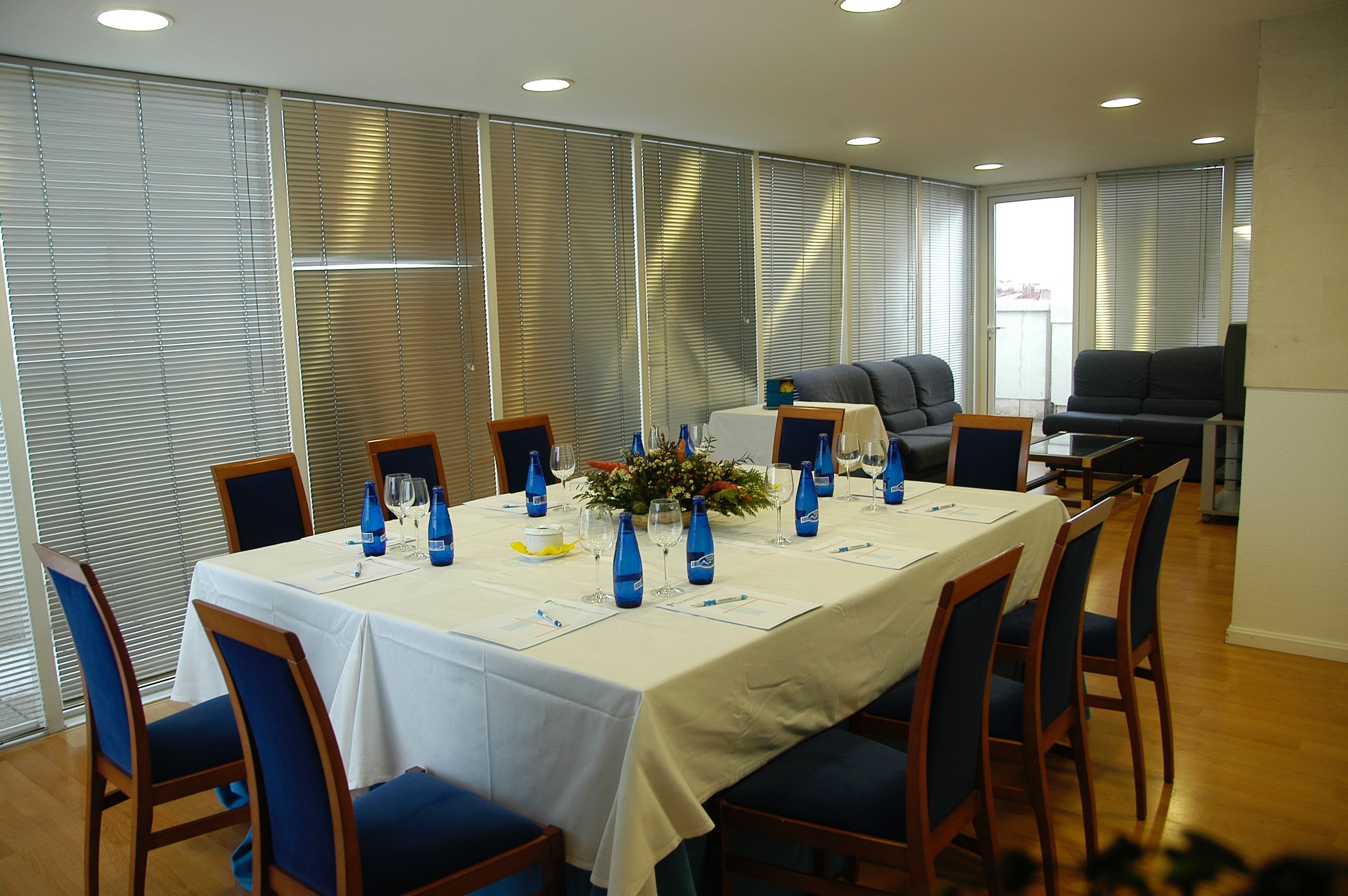 Un salón de conferencias con una larga mesa, sillas azules y un mantel blanco.