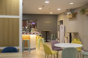 Un restaurant moderne avec un bar, des chaises colorées et une table blanche.