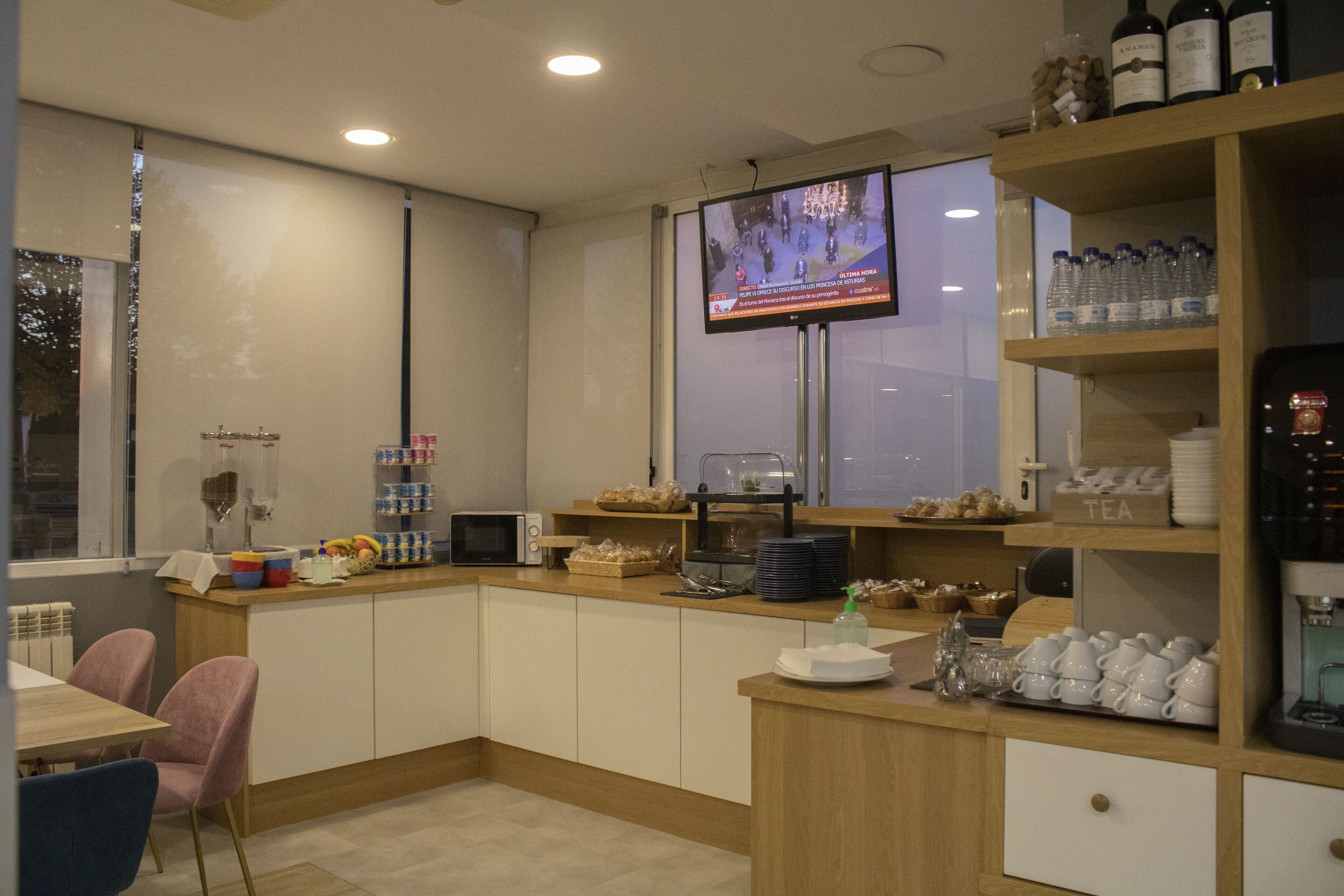 A modern kitchen with a flat-screen TV, a coffee machine, and a variety of food items on the counter.