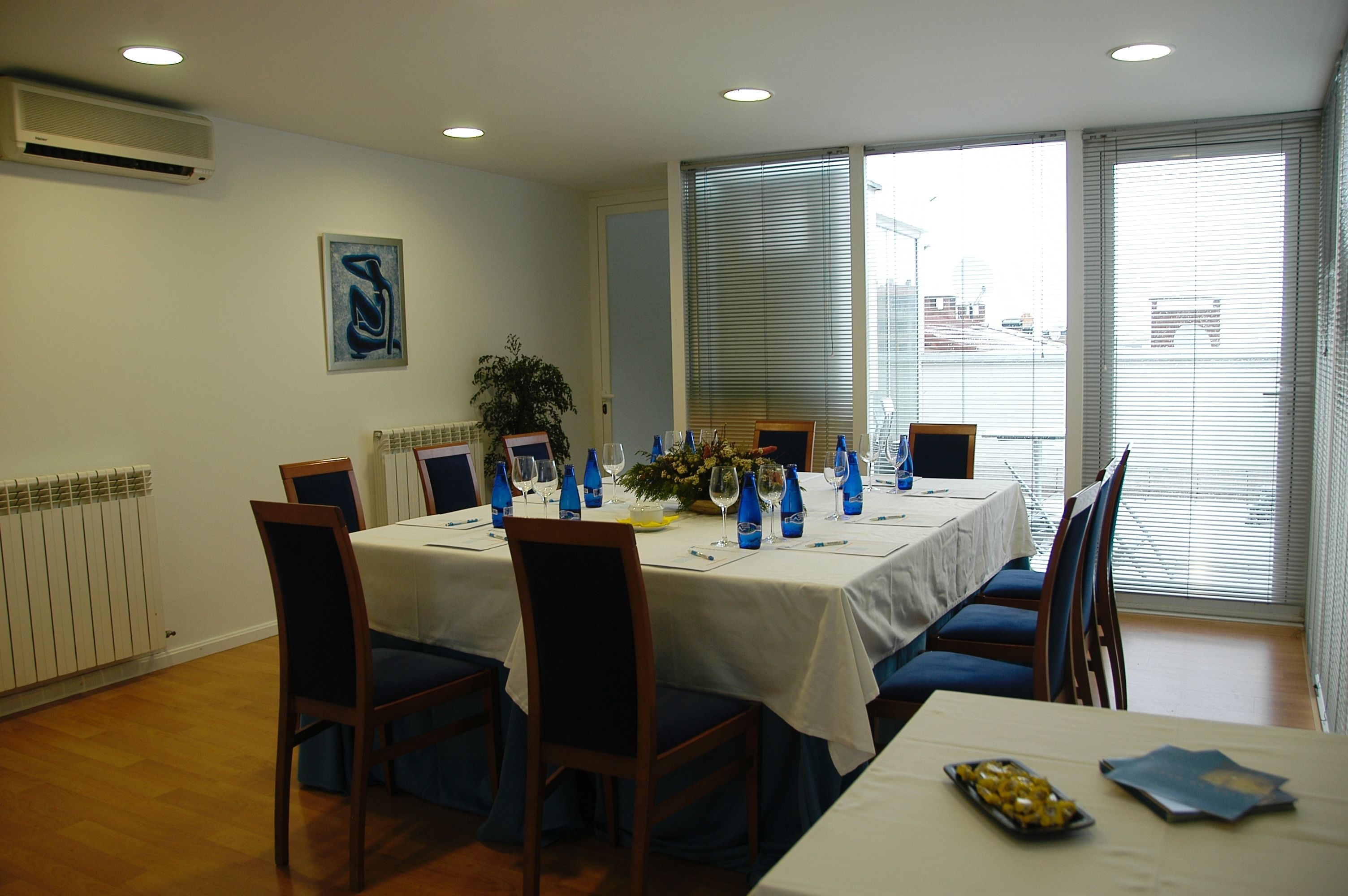 Een eethoek met een tafel voor vier personen, met blauwe stoelen, een witte tafelkleed en een decoratie bestaande uit bloemen en blauwe flessen.