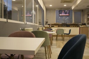 Un comedor moderno con mesas y sillas, un televisor montado en la pared y una encimera de cocina al fondo.