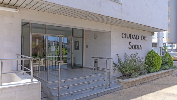 L’entrée d’un immeuble, avec une enseigne indiquant « CIUDAD DE SORIA », et un escalier menant à cette entrée.