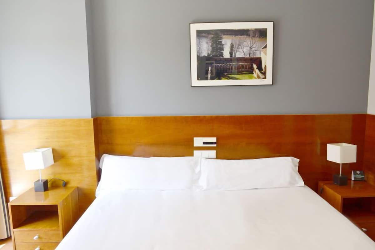 Ein Hotelzimmer mit einem großen Bett, einem hölzernen Kopfteil, zwei Nachttischen mit Lampen und einem gerahmten Bild an der Wand.