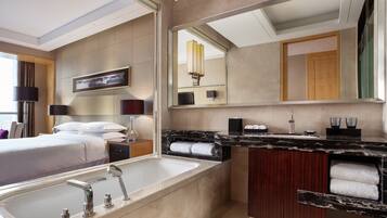 Un baño de hotel moderno con una bañera grande, un tocador con espejo y una cama con vistas.