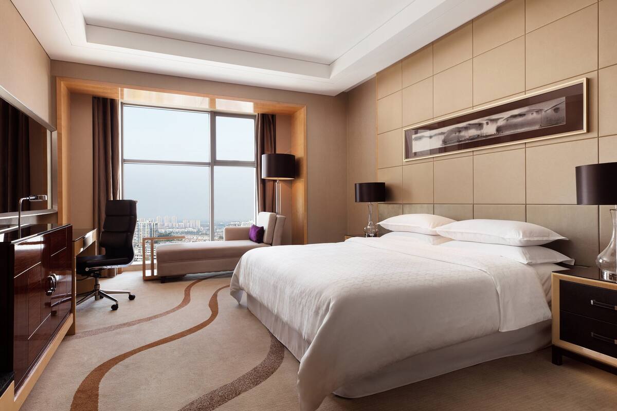 A hotel room with a large bed, a desk, a chair, and a view of the city.