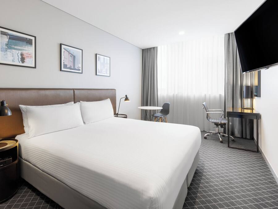 A hotel room with a large bed, a desk, a chair, and a television.