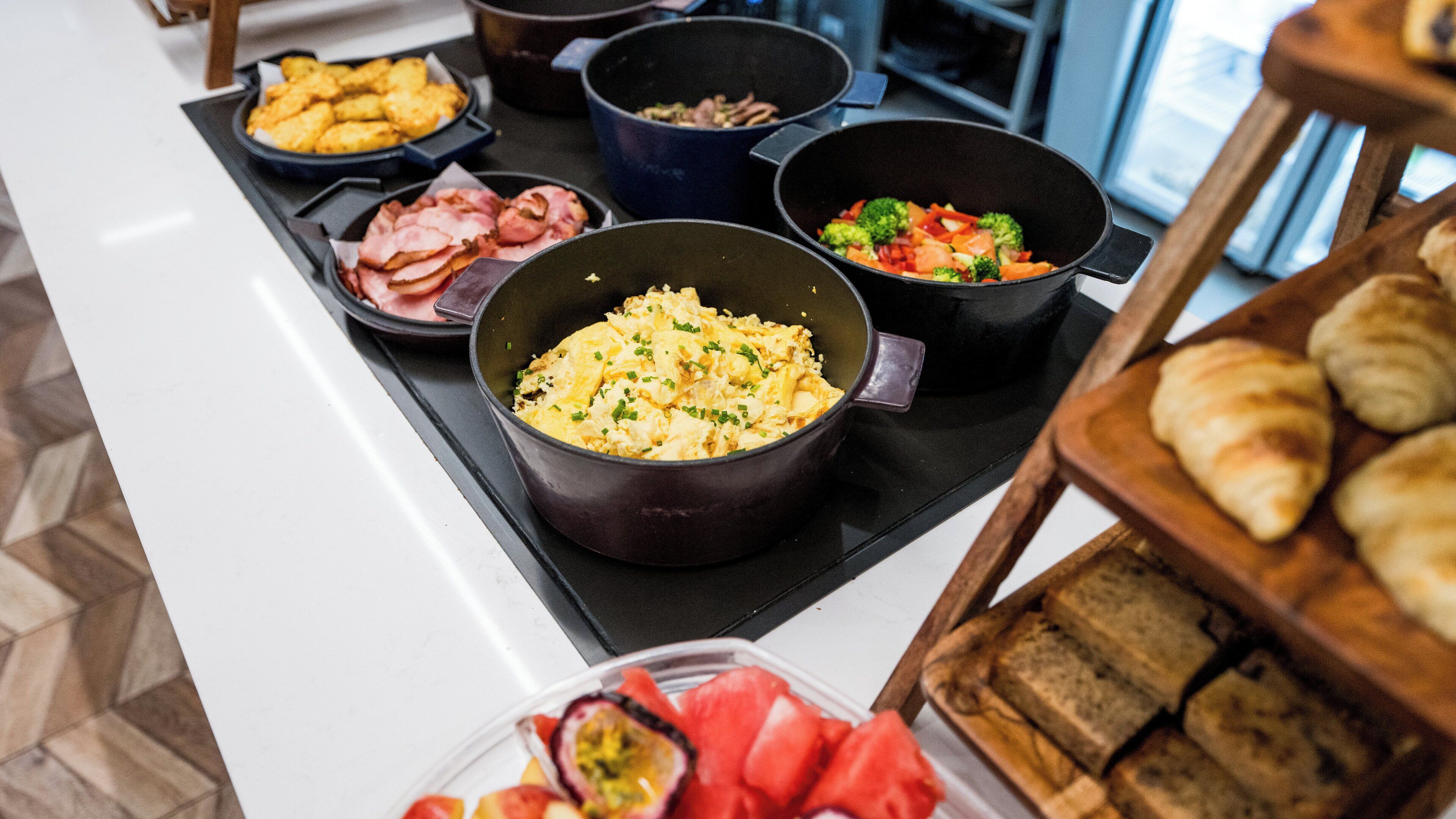 A buffet table with various dishes including scrambled eggs, vegetables, and pastries.