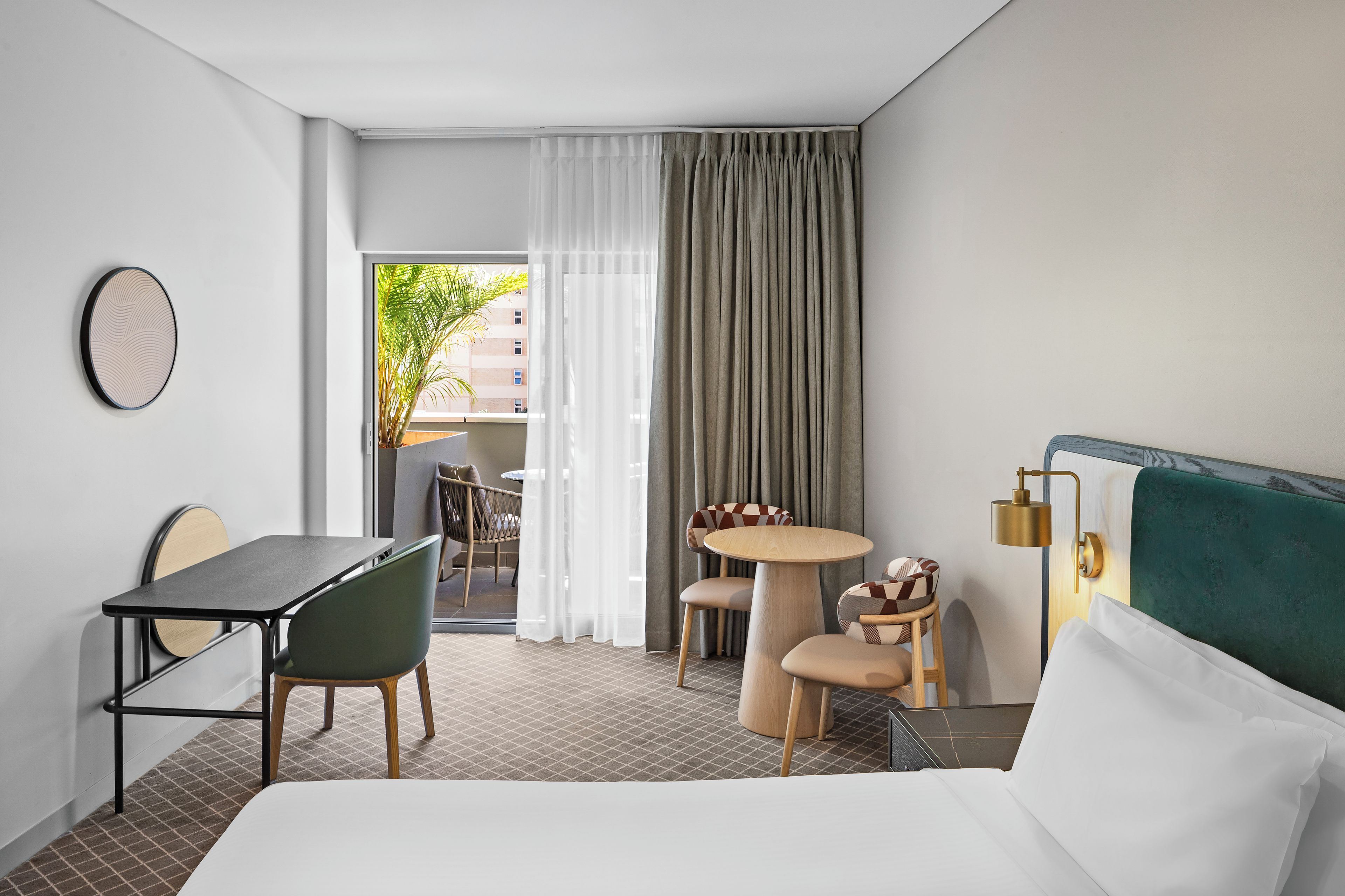 Une chambre d’hôtel avec un lit, un bureau, une chaise, une petite table et une vue sur l’extérieur.