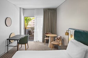 Habitación de hotel con cama, escritorio, silla, mesita y vistas al exterior.