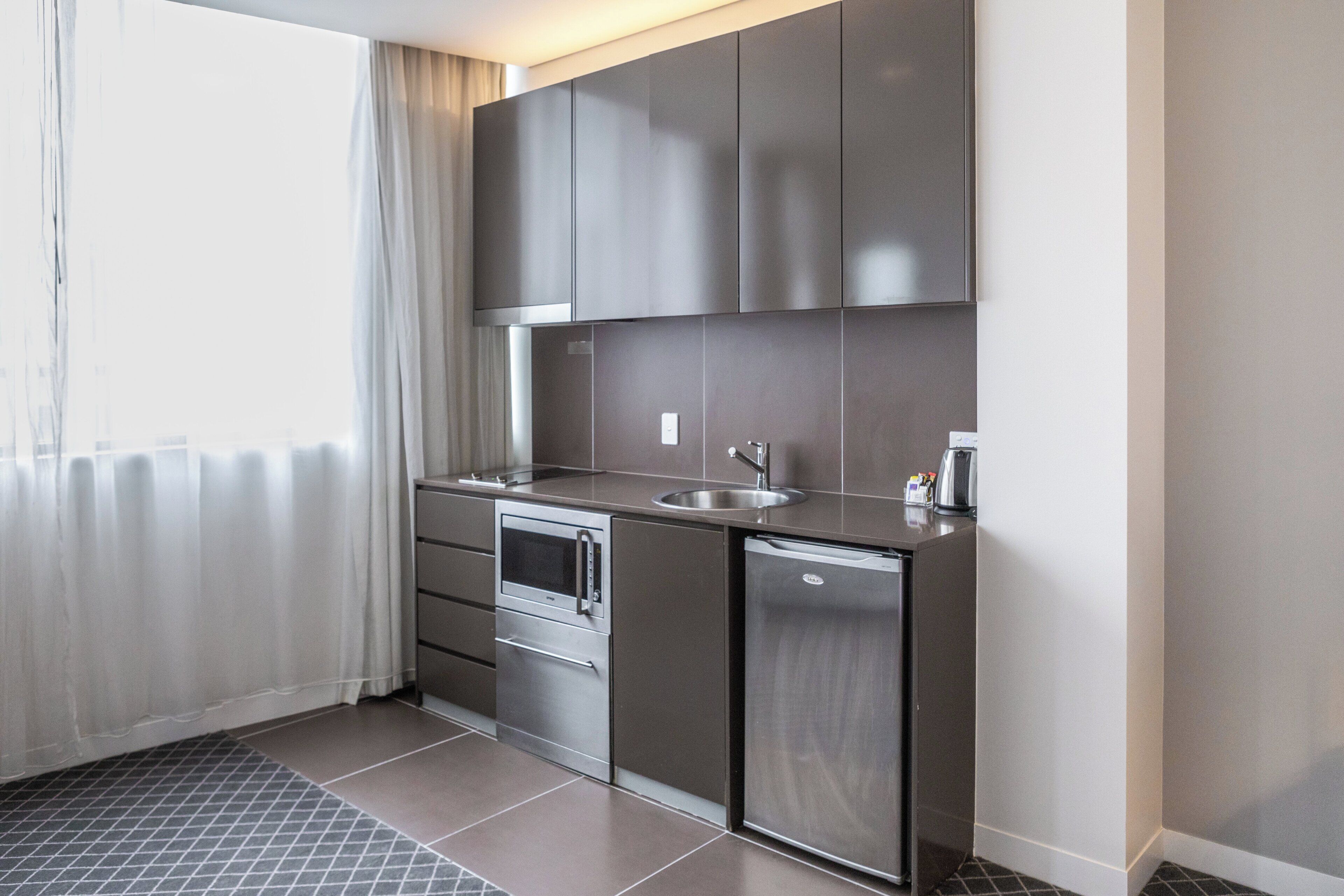 Una kitchenette compacta con horno integrado, un lavamanos y un refrigerador pequeño.
