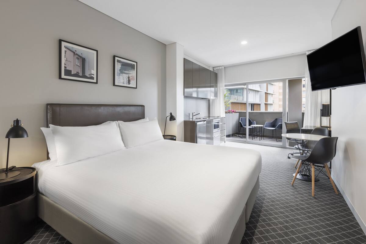 A modern hotel room with a large bed, a desk, and a flat-screen TV.