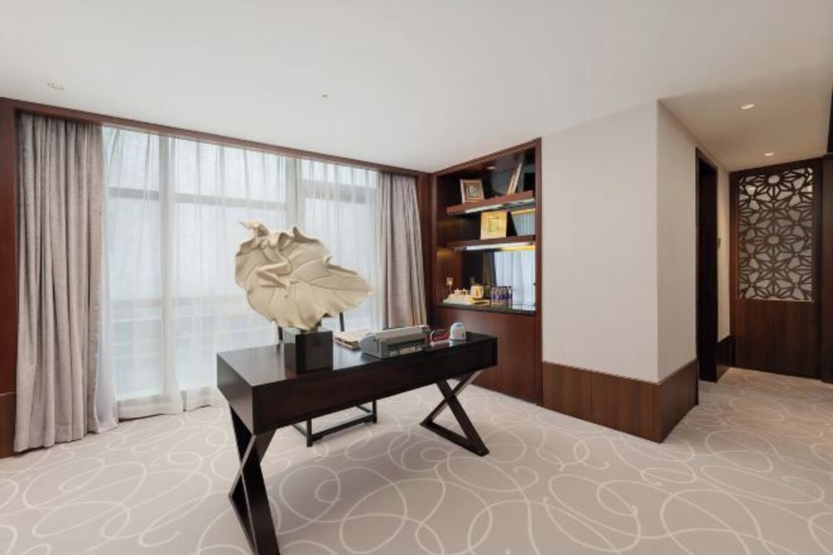 Habitación de hotel con escritorio, una escultura decorativa, estantería y alfombra estampada.