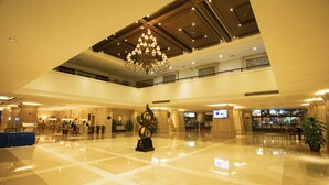 Een ruime lobby met een hoog plafond, een kroonluchter en een centraal geplaatst sculptuur.