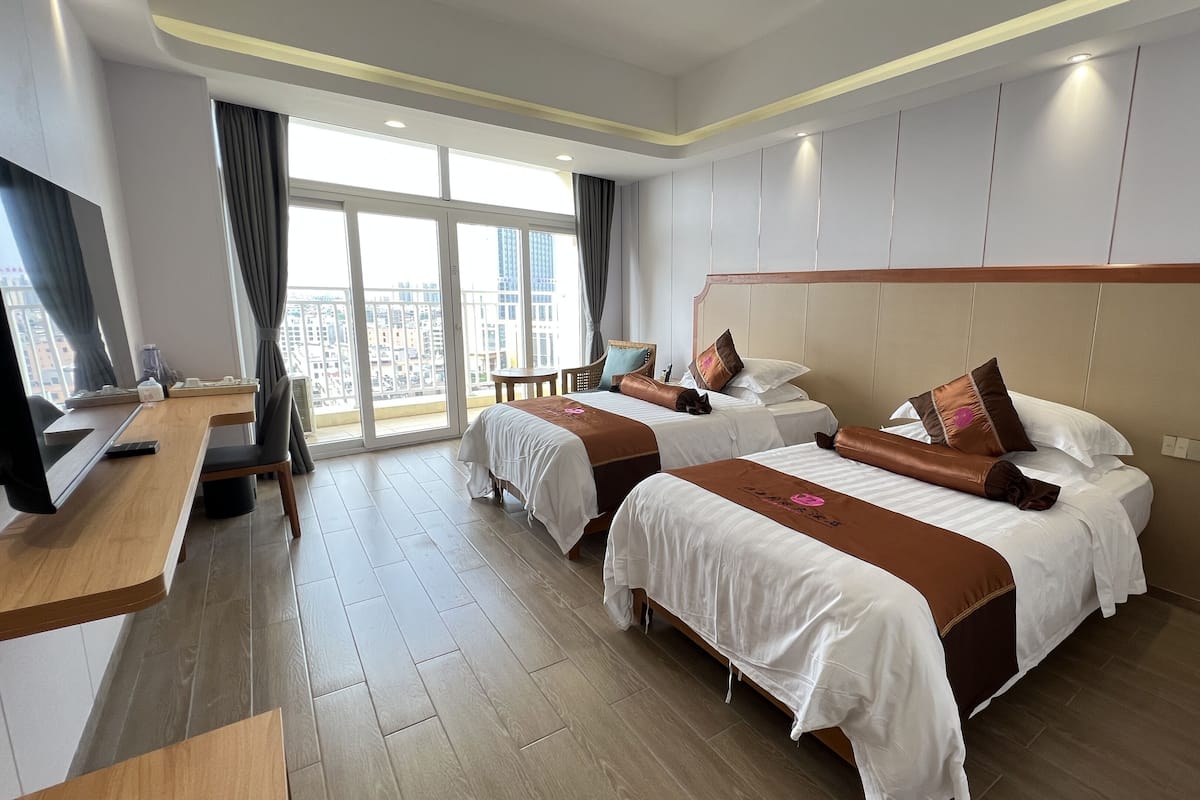 A hotel room with two beds, a desk, and a large window with curtains.