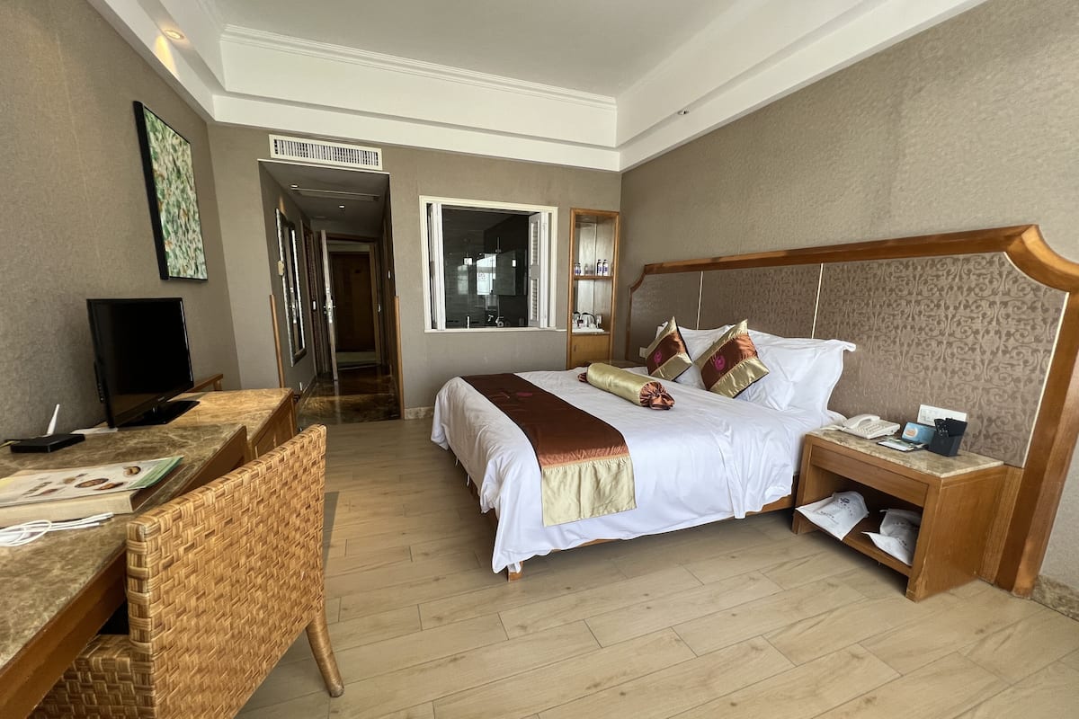A hotel room with a bed, bedside table, TV, and a desk with a chair.