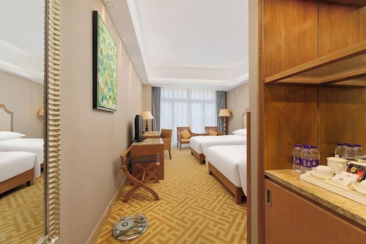A hotel room with two beds, a desk, a chair, a TV, and a minibar.