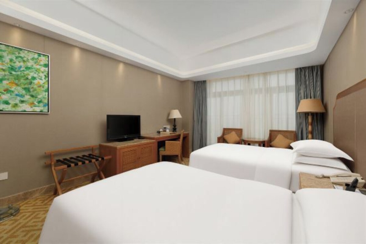 Habitación de hotel con dos camas, un escritorio, televisor, lámpara y un cuadro en la pared.