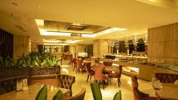 En modern hotellobby med en central sittgrupp, en receptionsdisk och ett kök som syns i bakgrunden.