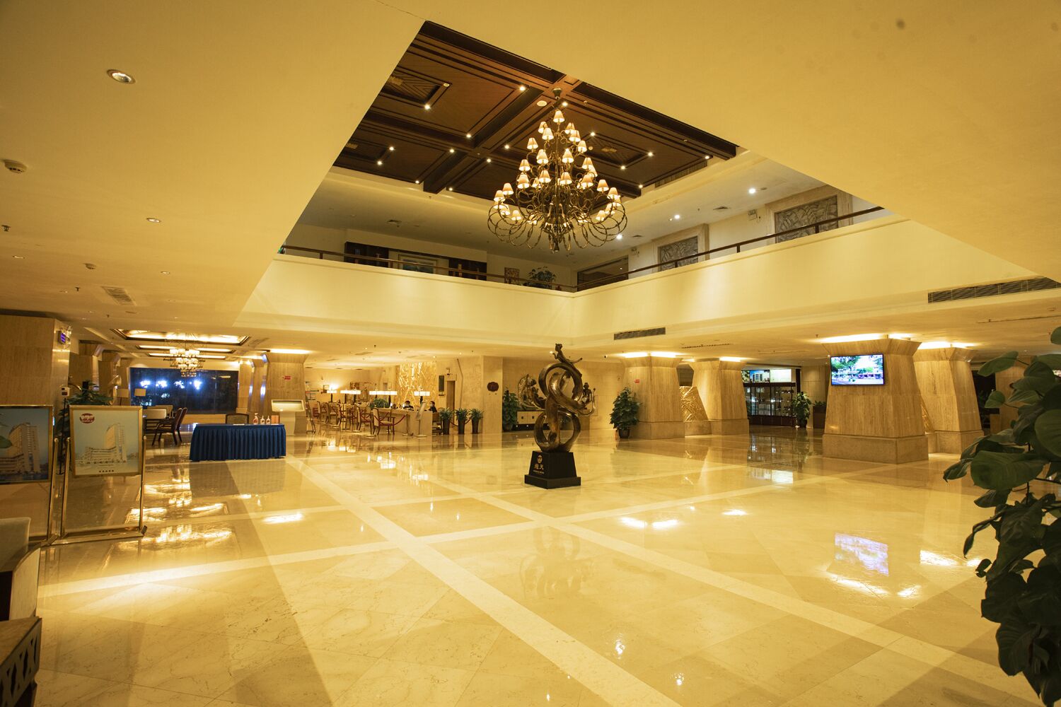 A spacious lobby with a high ceiling, a chandelier, and a reception desk.