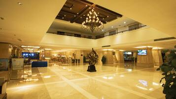 A spacious lobby with a high ceiling, a chandelier, and a reception desk.