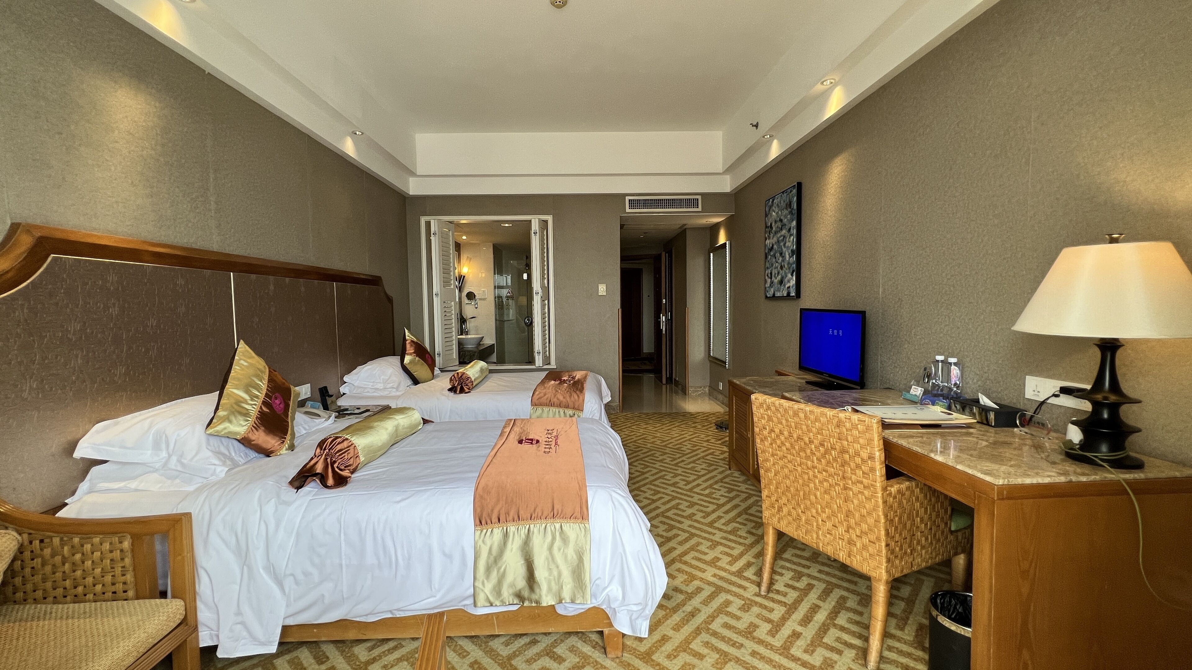 A hotel room with two beds, a desk, a chair, a television, and a lamp.