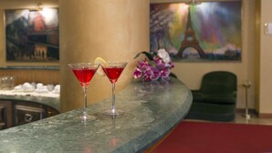 A bar area with two red cocktails on a marble countertop, a green chair, and a painting of the Eiffel Tower in the background. - Hotel de Paris (Terni)