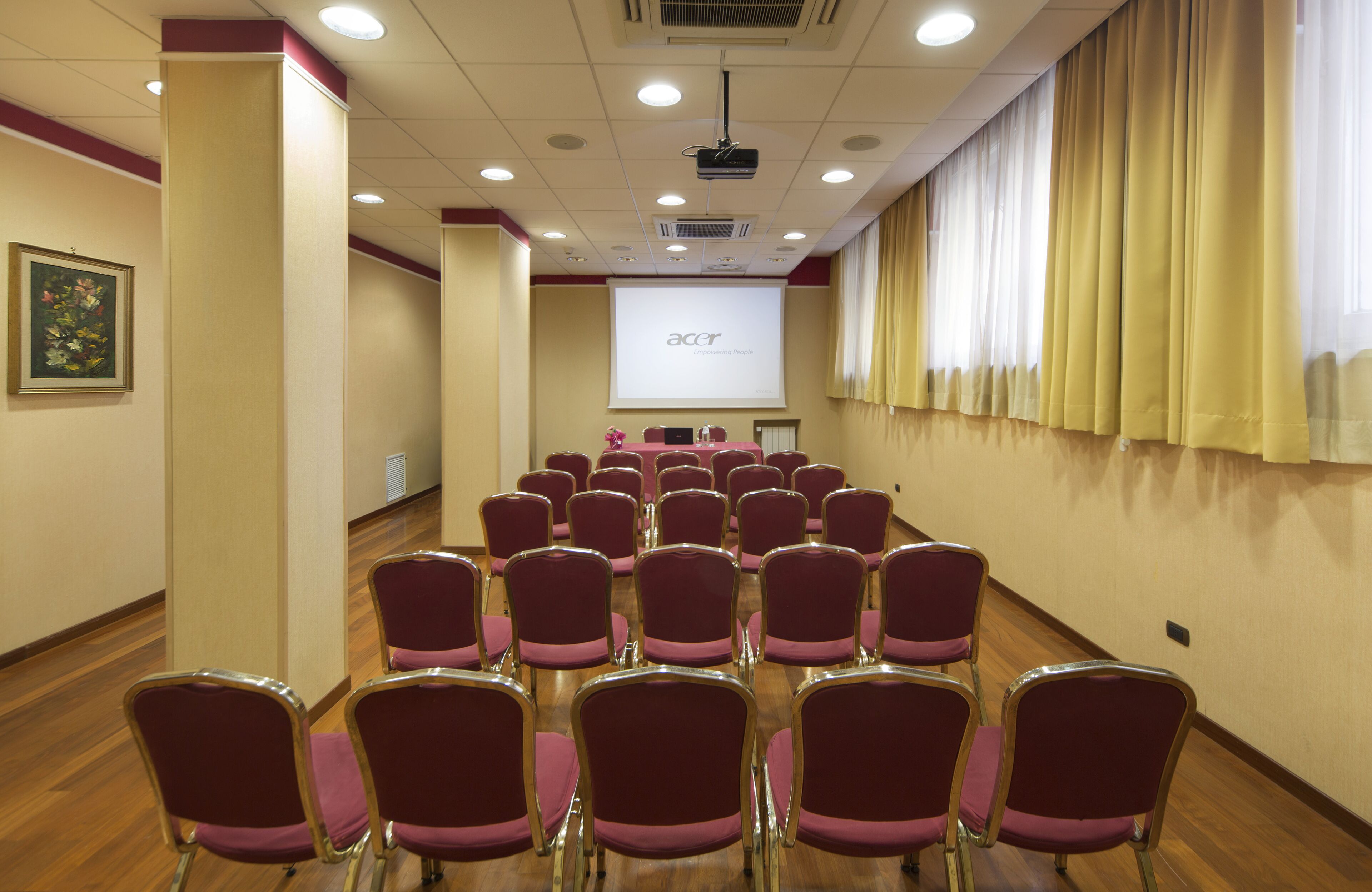 Un salón de conferencias con filas de sillas, una pantalla de proyector y un atril.