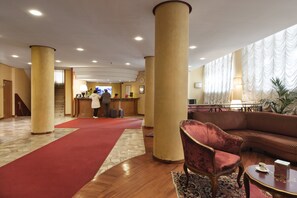 Vestíbulo de hotel con alfombra roja, una recepción, un sofá y una silla.