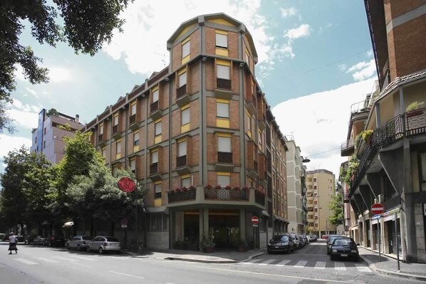 Un hotel de varios pisos con entrada en esquina, balcones y vista a la calle.