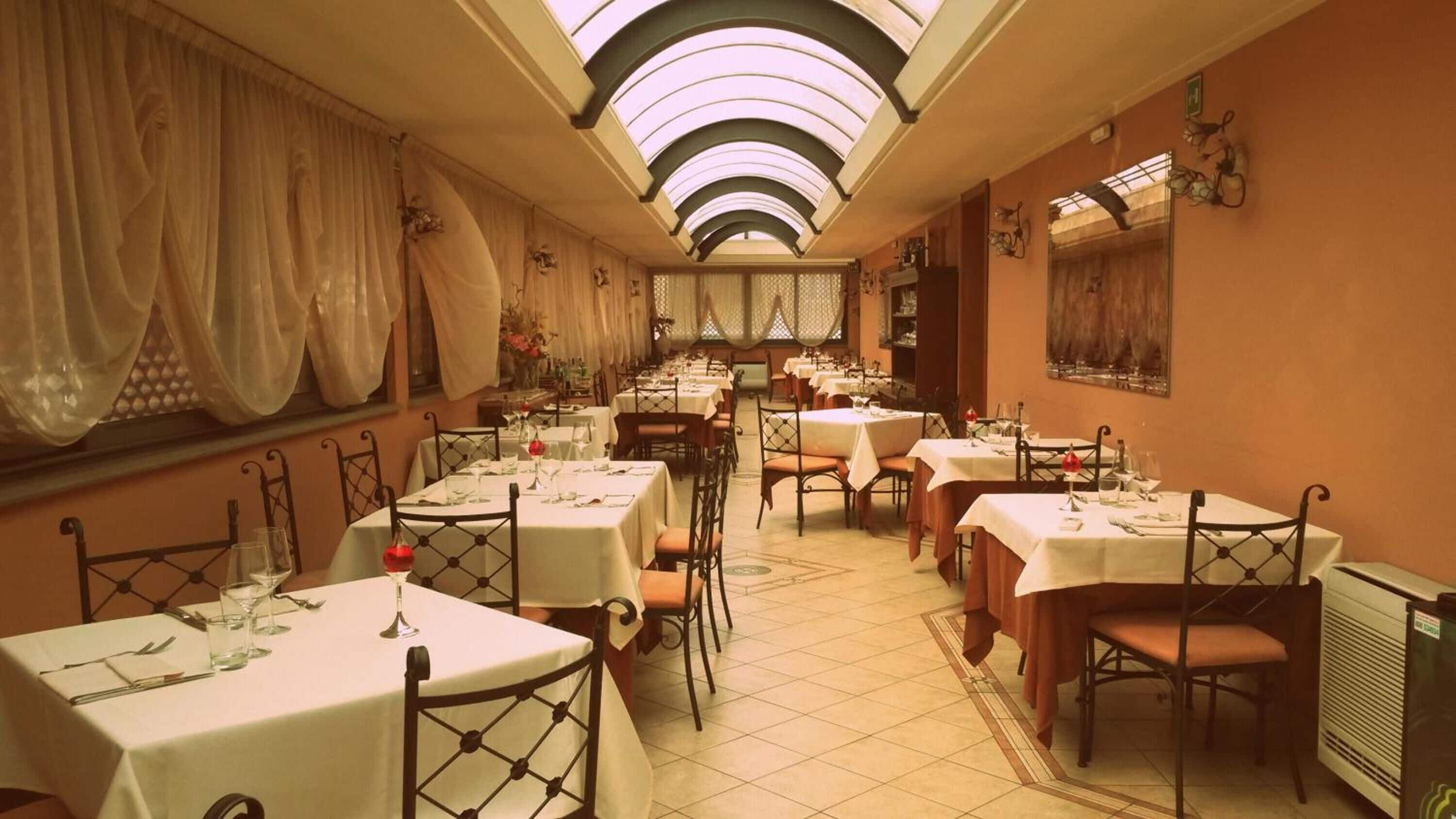 Un restaurante con varias mesas, cada una con manteles blancos y copas de vino tinto.