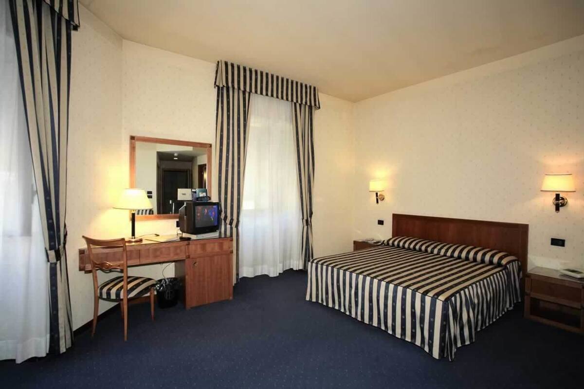A hotel room with a bed, a desk with a chair, a television, and two bedside lamps.