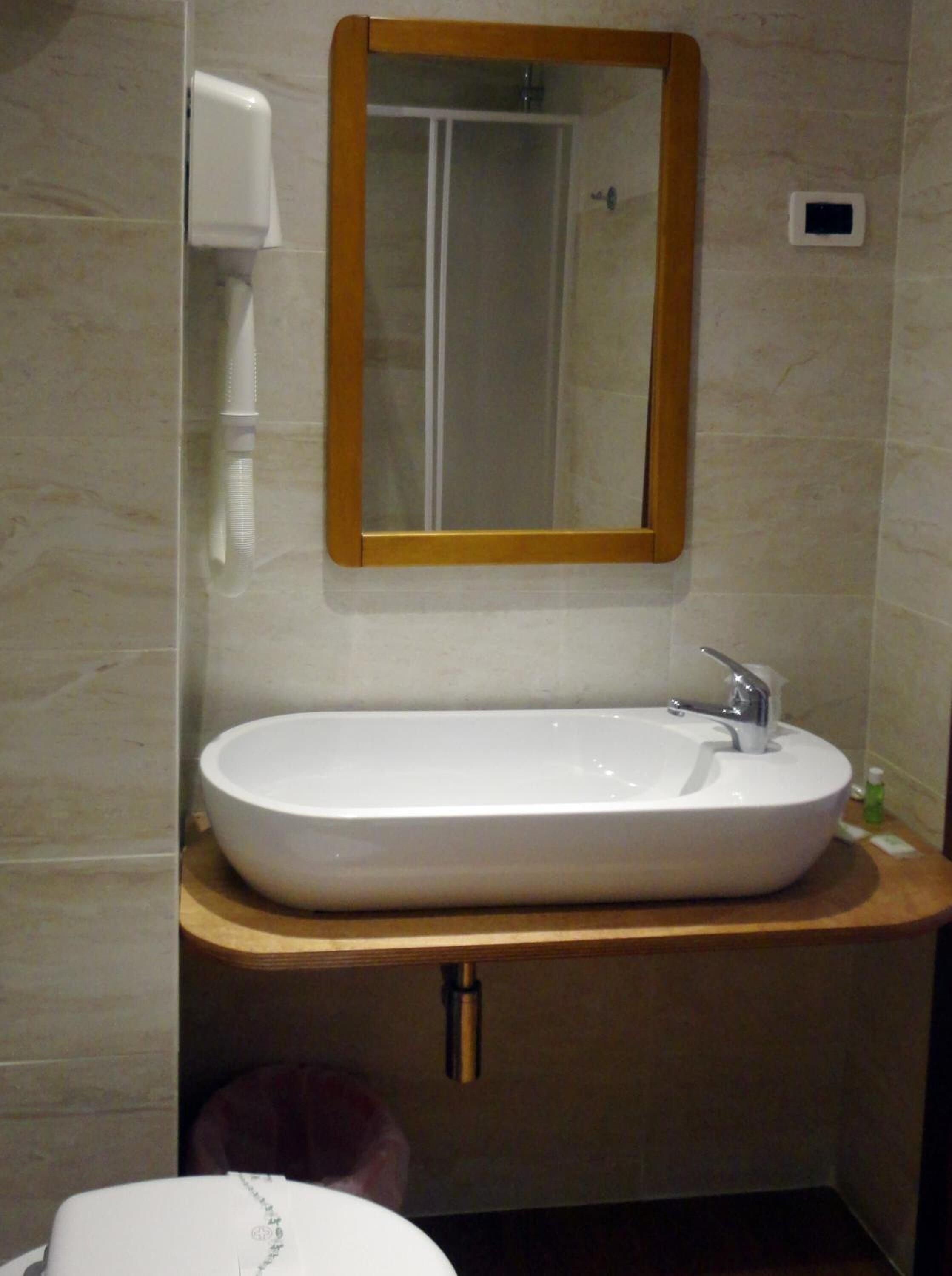 Ein Badezimmer mit einem weißen Waschbecken, einer Holzauskład, einem Spiegel und einer Handbrause.