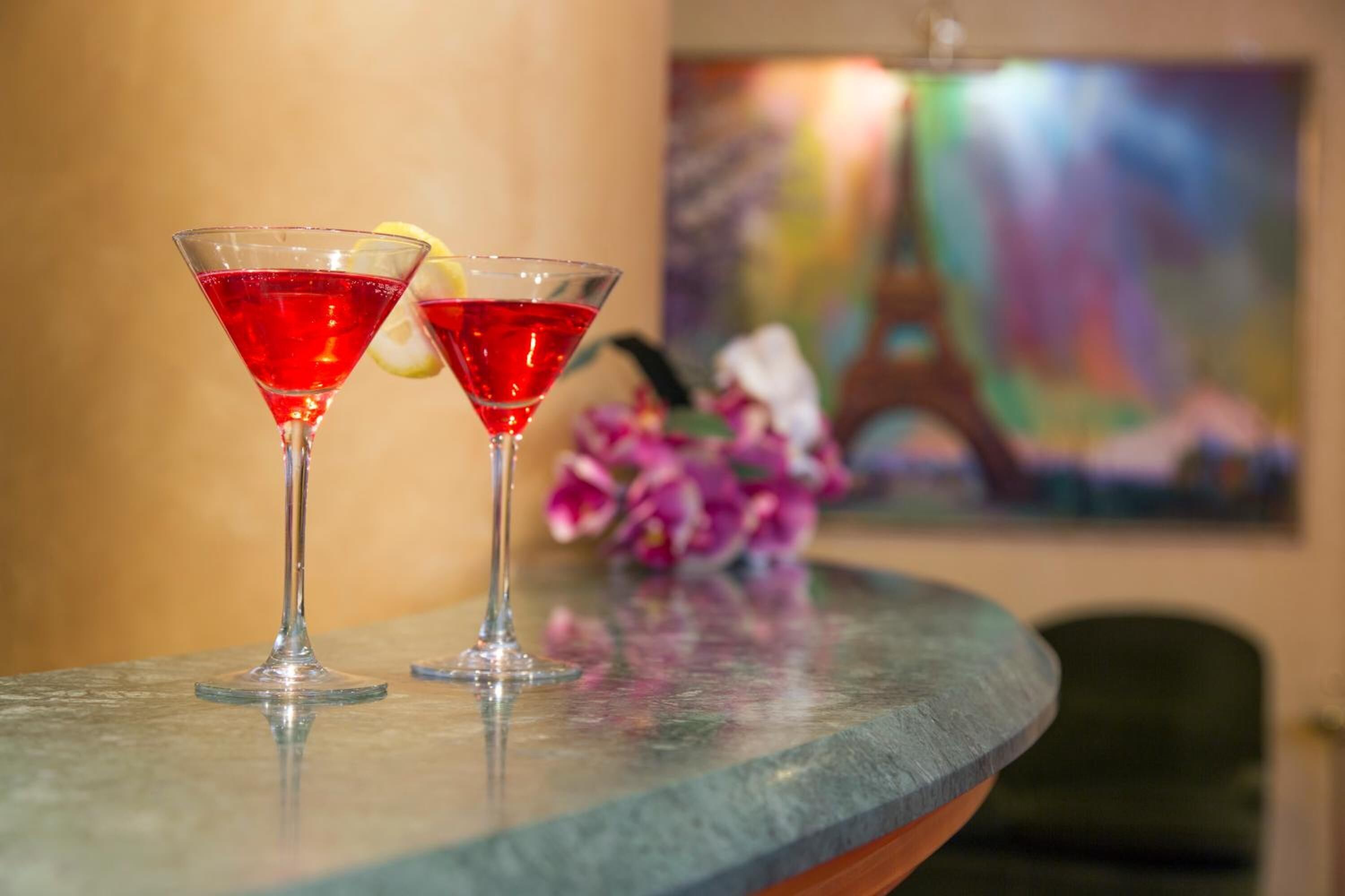 Two red cocktails on a marble bar counter with a painting in the background.