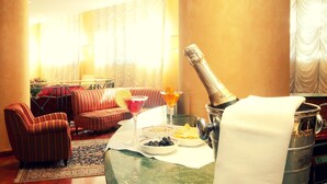 A well-lit living room with a sofa, armchairs, a table with a bottle of champagne, a martini glass, and a bowl of snacks. - Hotel de Paris (Terni)