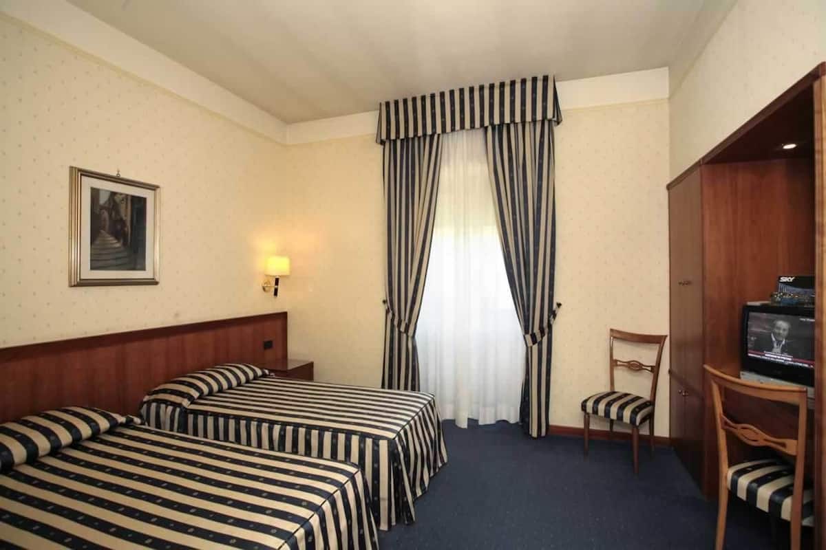 A hotel room with two beds, a television, a chair, and a large window with curtains.