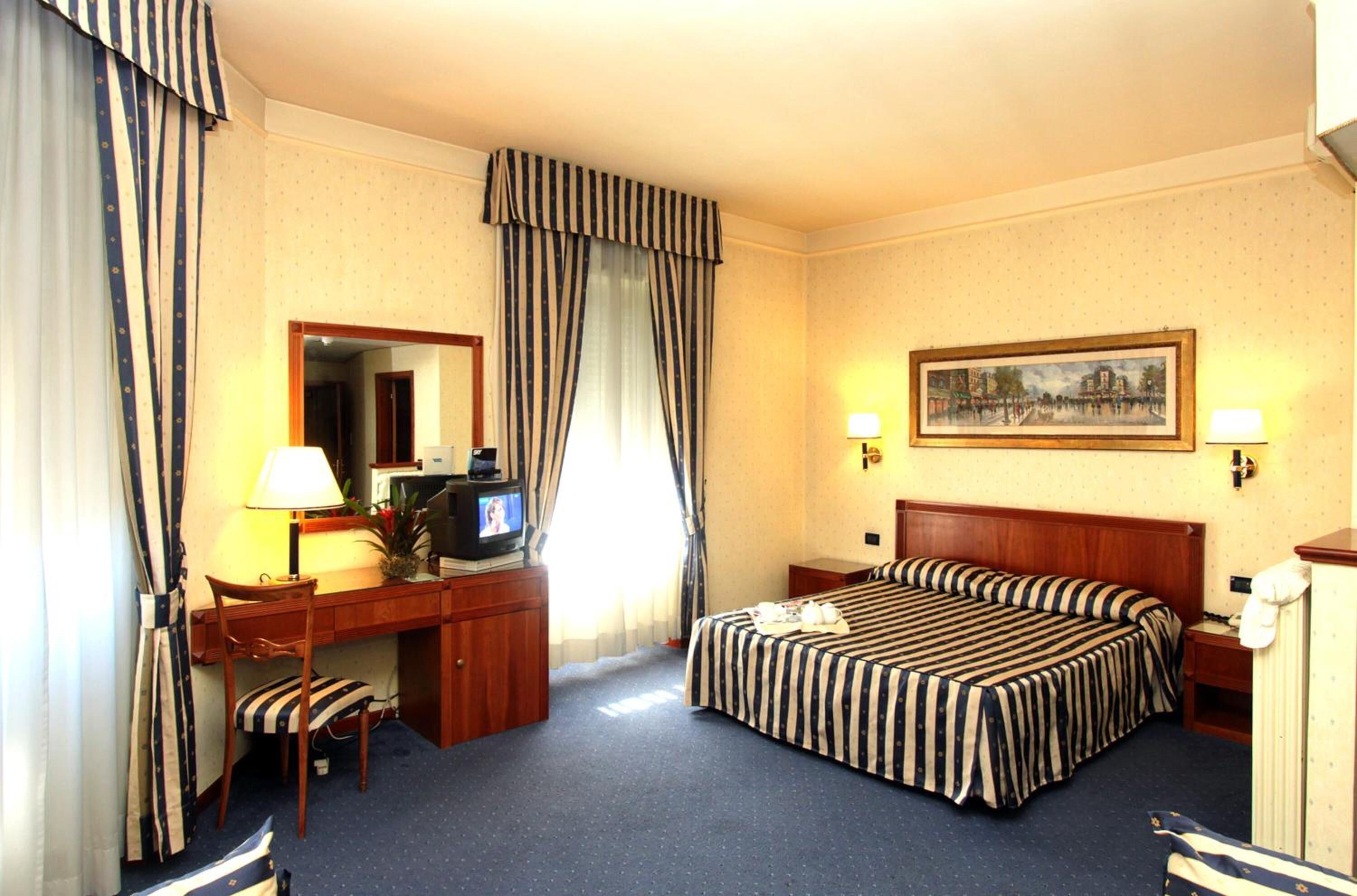 A hotel room with a bed, desk, chair, TV, and two bedside lamps.