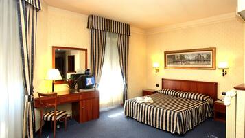 A hotel room with a bed, desk, chair, TV, and two bedside lamps.