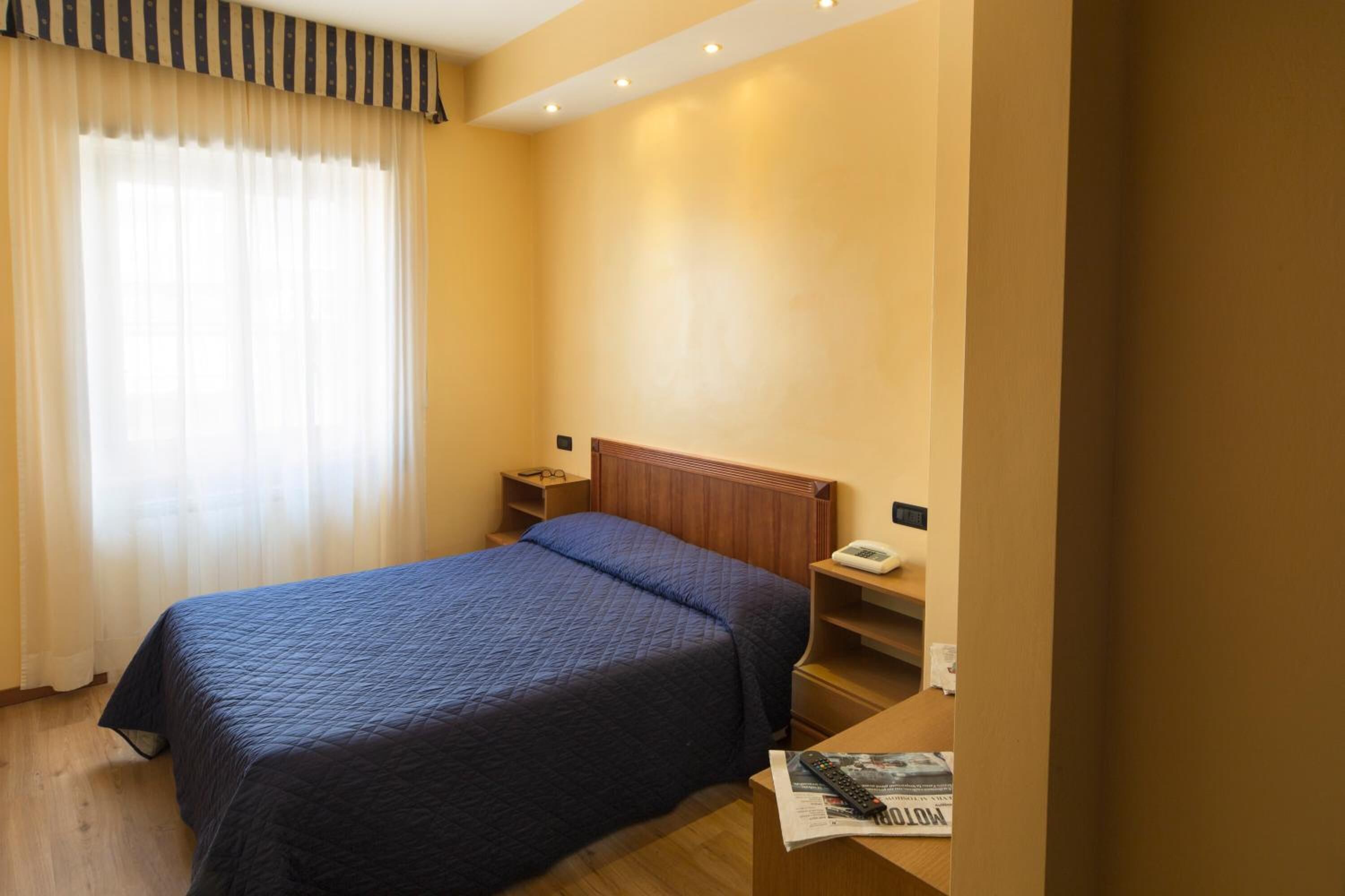 A hotel room with a bed, bedside tables, a nightstand, a telephone, and a window with curtains.