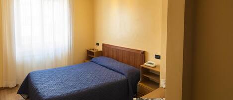 A hotel room with a bed, bedside tables, a nightstand, a telephone, and a window with curtains.