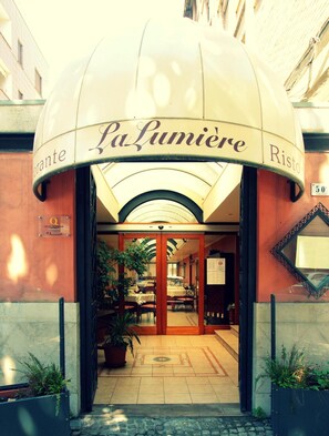 La entrada a La Lumìere Ristorante, con un porche cubierto, plantas en macetas y piso de baldosas.