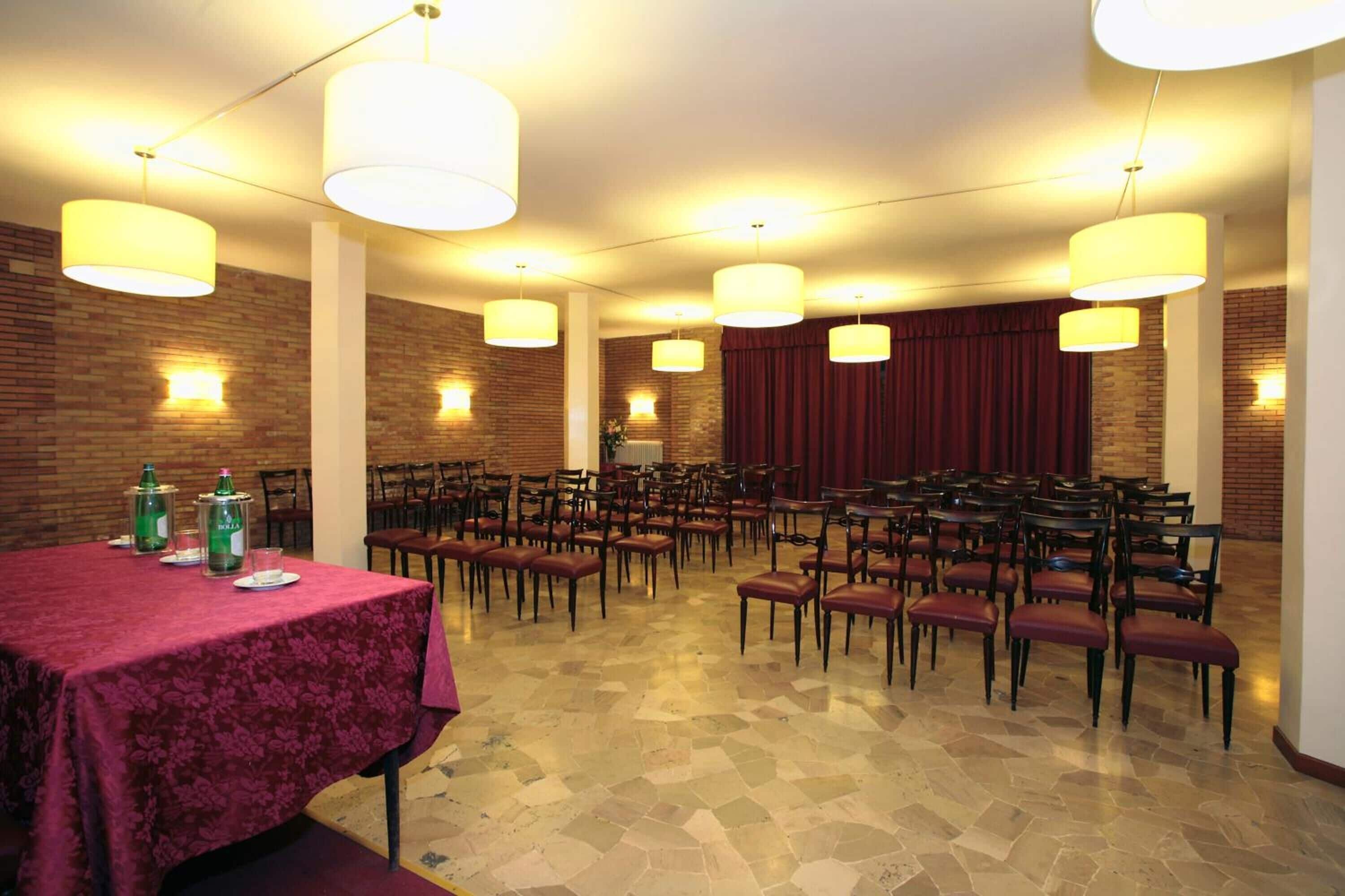 Un salón de conferencias con una larga mesa, varias sillas e iluminación colgante.