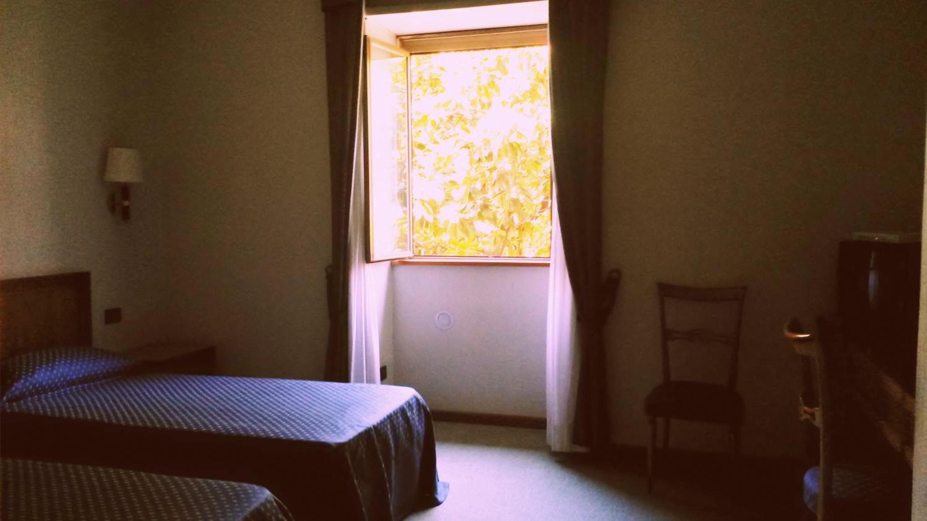 Una habitación con dos camas, una silla, un televisor y una ventana con cortinas.