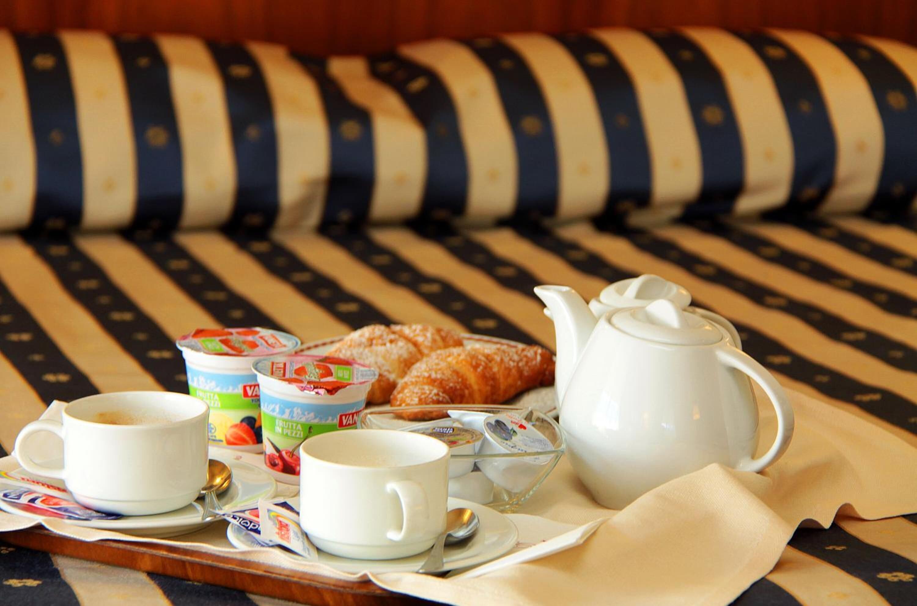 A breakfast tray with croissants, yogurt, and a teapot on a striped sofa.