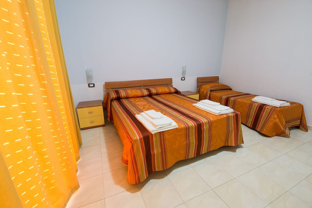 Habitación de hotel con dos camas, una mesita de noche y una ventana con persianas.