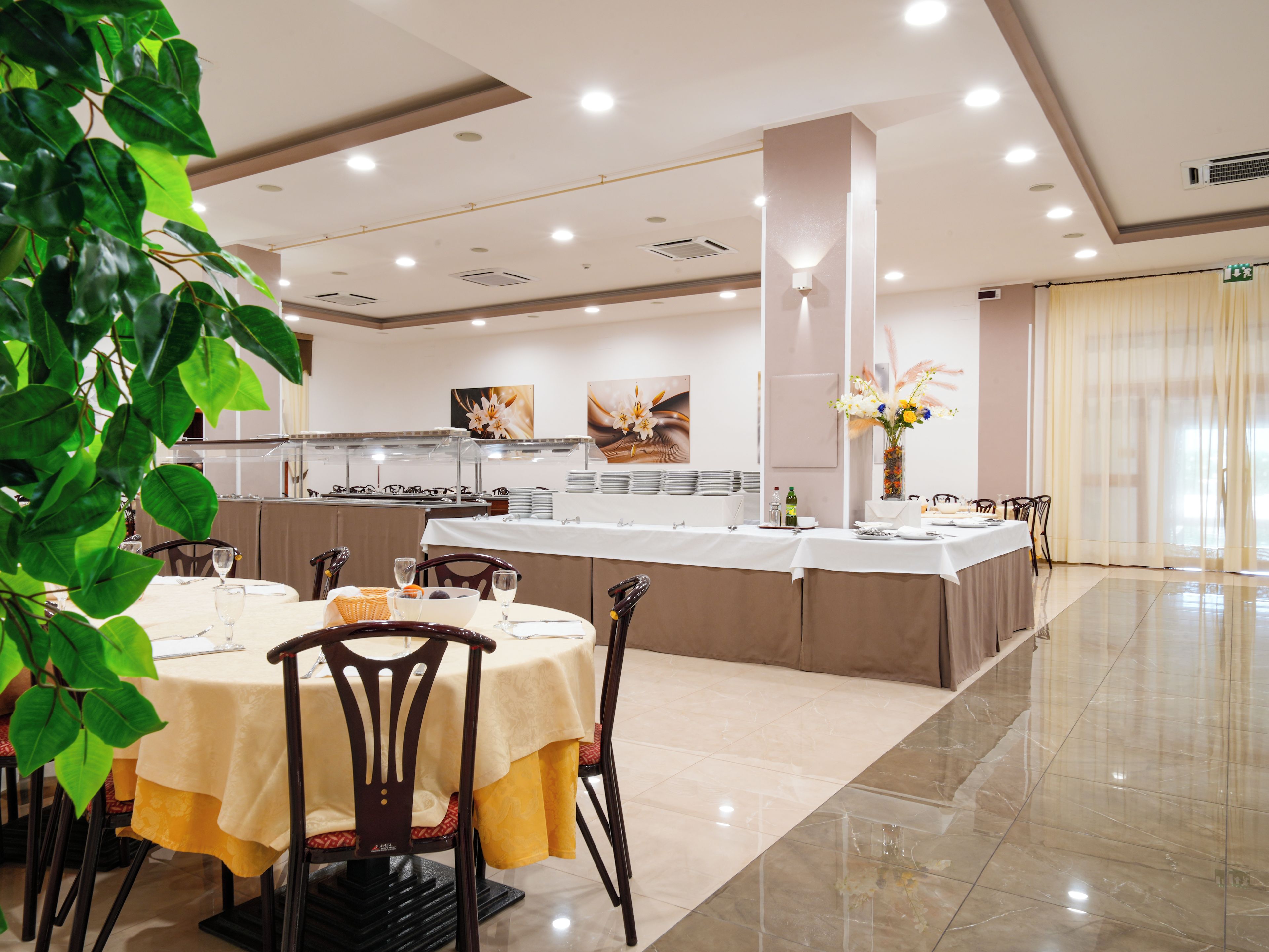 Una sala ristorante con un'area buffet, tavoli e sedie, e una pianta decorativa.