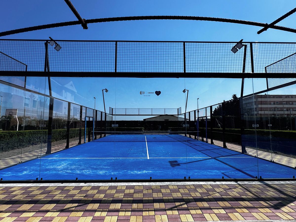 An indoor tennis court with a net, surrounded by a fence, and a clear sky above.