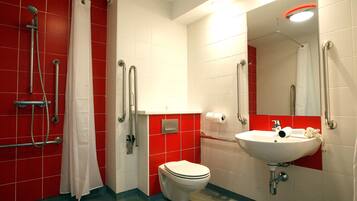 A bathroom with a white toilet, red tiled walls, a white sink, and a shower area with grab bars.